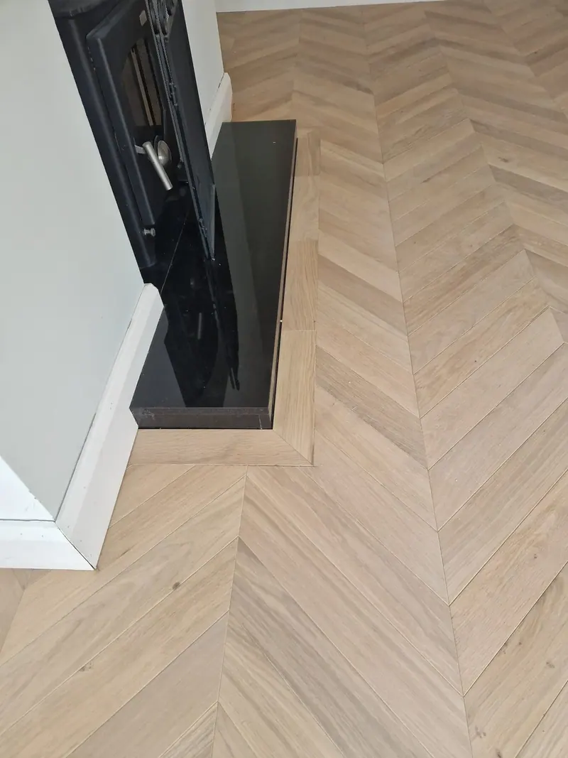 Pale chevron floor meeting a dark unit at the foot of the stairs