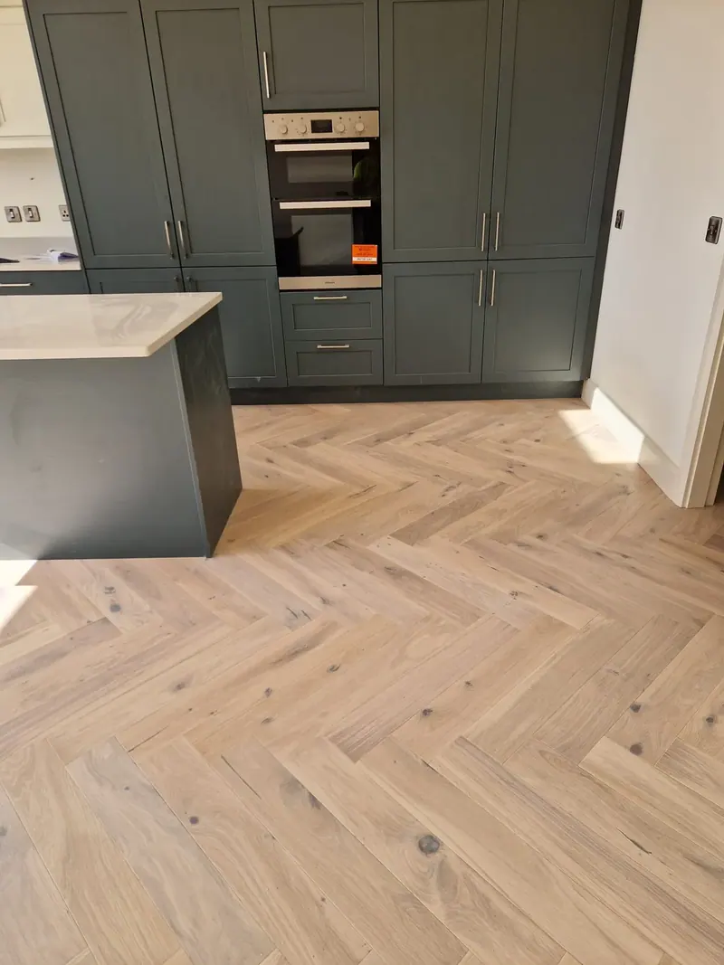Light herringbone floor in a kitchen with dark green units