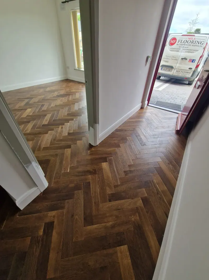 Dark herringbone floor in an entrance hall with the Mila Flooring van outside the front door